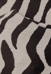 Tissu tricoté présentant un motif à rayures de zèbre en brun foncé sur un fond beige clair, mettant en valeur la texture et les couleurs contrastées.
