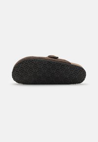 Pantofii slip-on din suede maro, cu o talpă din cauciuc negru ce prezintă un model texturat. Include un detaliu decorativ cu cataramă pe lateral.