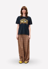 Zwart graphic t-shirt met een gele en oranje kroonprint, gecombineerd met bruin geruit wijde broekspijpen en gele instappers.