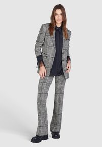 Black and white checked suit with a tailored blazer and flared trousers, featuring a sleek black top with sheer sleeve accents.