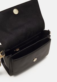 Bolso de shoulder de cuero negro con textura suave, herrajes dorados y un interior espacioso que cuenta con un bolsillo con cremallera y dos secciones abiertas.