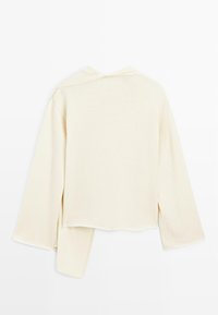 Pull en tricot crème avec des manches longues, design court et fentes sur les côtés. Texture lisse avec un col rond et sans fermetures visibles.