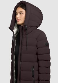 Puffer jacket in dark burgundy with a large hood, quilted texture, silver lining, and a zippered front. Features black hardware accents.