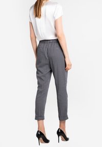 Black and white checkered trousers with a tapered fit and elastic waistband, paired with a simple white short-sleeve blouse.