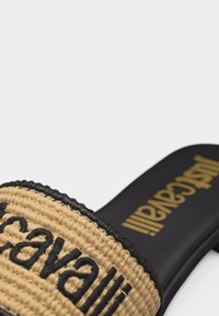 Μαύρο σανδάλι με πλατφόρμα και μπεζ πλεγμένο λουρί που έχει μαύρο κεντημένο το κείμενο "Stradivarius", και χρυσή επωνυμία "Stradivarius" στη σόλα.