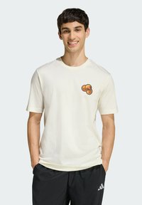 Krémové tričko s krátkymi rukávmi a okrúhlym výstrihom, na ľavej hrudi s vyšitým dizajnom pozostávajúcim z troch oranžových kruhov.