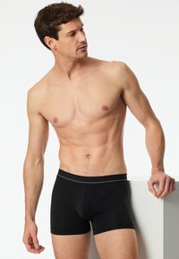 Boxer aderenti neri con un morbido elastico in vita caratterizzato da una sottile striscia grigia. Il tessuto sembra liscio e aderente. Il modello posa su uno sfondo bianco.
