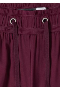 Gros plan d'une ceinture élastique bordeaux avec des cordons passés à travers des œillets métalliques sur un pantalon en tissu.