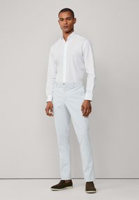 Camisa blanca de botones con cuello puntiagudo, combinada con pantalones claros azules y zapatos marrones de piel. Diseño simple y estilo ajustado.