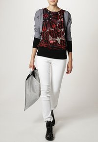 Haut à manches longues multicolore avec des motifs floraux et de papillons, associé à un pantalon skinny blanc et un sac fourre-tout argenté texturé.