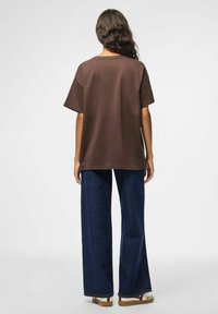 T-shirt marrone oversize con maniche corte. Abbinato a pantaloni jeans a gamba larga in denim scuro. Materiale morbido, vestibilità casual, senza motivi visibili.