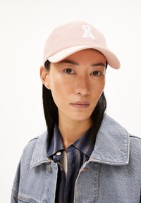 Lichtroze baseballpet met een geborduurde witte letter "A". Van katoen, met een gebogen rand, gedragen met een denimjack en een gestreept shirt.