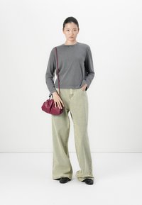 Woman wearing a gray long-sleeve shirt, light wide-leg jeans, black shoes, and holding a small burgundy shoulder bag.