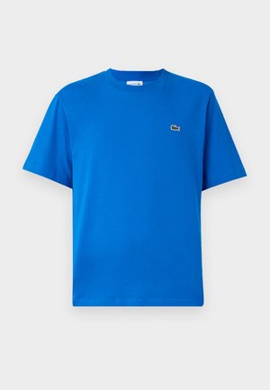 Sininen puuvillapaita lyhyillä hihoilla, pyöreällä pääntiellä ja vihreällä brodeeratulla logolla vasemmassa rintakohdassa. Liukas rakenne, klassinen istuvuus.