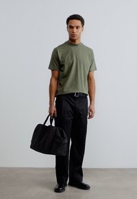 Κοντομάνικο μπλουζάκι σε ελιά πράσινο, μαύρο παντελόνι και μαύρη διπλή τσάντα. Λείο ύφασμα, άνετη εφαρμογή, μινιμαλιστικός σχεδιασμός και μανίκια μέτριου μήκους.