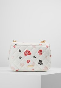 Prošívaná bílá kabelka s růžovými vzory v červené, růžové a černé barvě. Zlaté kovové prvky a zipové uzávěr na vrchu. Kompaktní obdélníkový tvar.