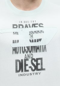 Άσπρο T-shirt με στρωματοποιημένο κείμενο που περιλαμβάνει τα «BRAVES», «AUTOSOMATIX» και «DIESEL INDUSTRY» σε μαύρο και ένα μεγάλο λευκό ραμμένο λογότυπο.