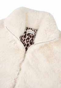 Lažno krzno vanjska odjeća u krem boji s mekom teksturom. Zatvaranje na patentni zatvarač i obloga u smešastoj leopard print. Etiketa glasi "OH APRIL."
