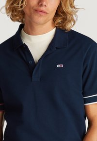 Polo de algodón color navy, con un cierre de tres botones, acentos a rayas blancas y rosas en las mangas, y logo bordado en el pecho.