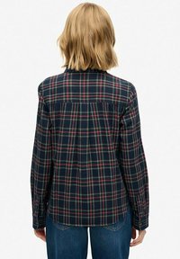 Plaid flannel shirt in navy with red, green, and yellow patterns. Long sleeves, cuffed, and a yoke detail on the back. Casual fit.