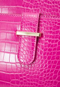 Jasnoróżowa torebka z teksturą wzoru krokodyla, wyposażona w złote zapięcie i dopasowany skórzany pasek.