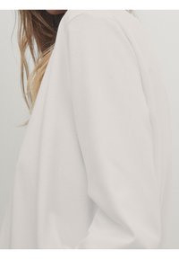 Hvid sweatshirt med en blød tekstur og løs pasform, med en rund halsudskæring og let nedfaldende skuldre. Minimalistisk design.