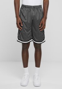 Shorts rayés noir et blanc avec une texture en maille, taille élastique et bord blanc à l'ourlet, associés à des baskets blanches et des chaussettes.