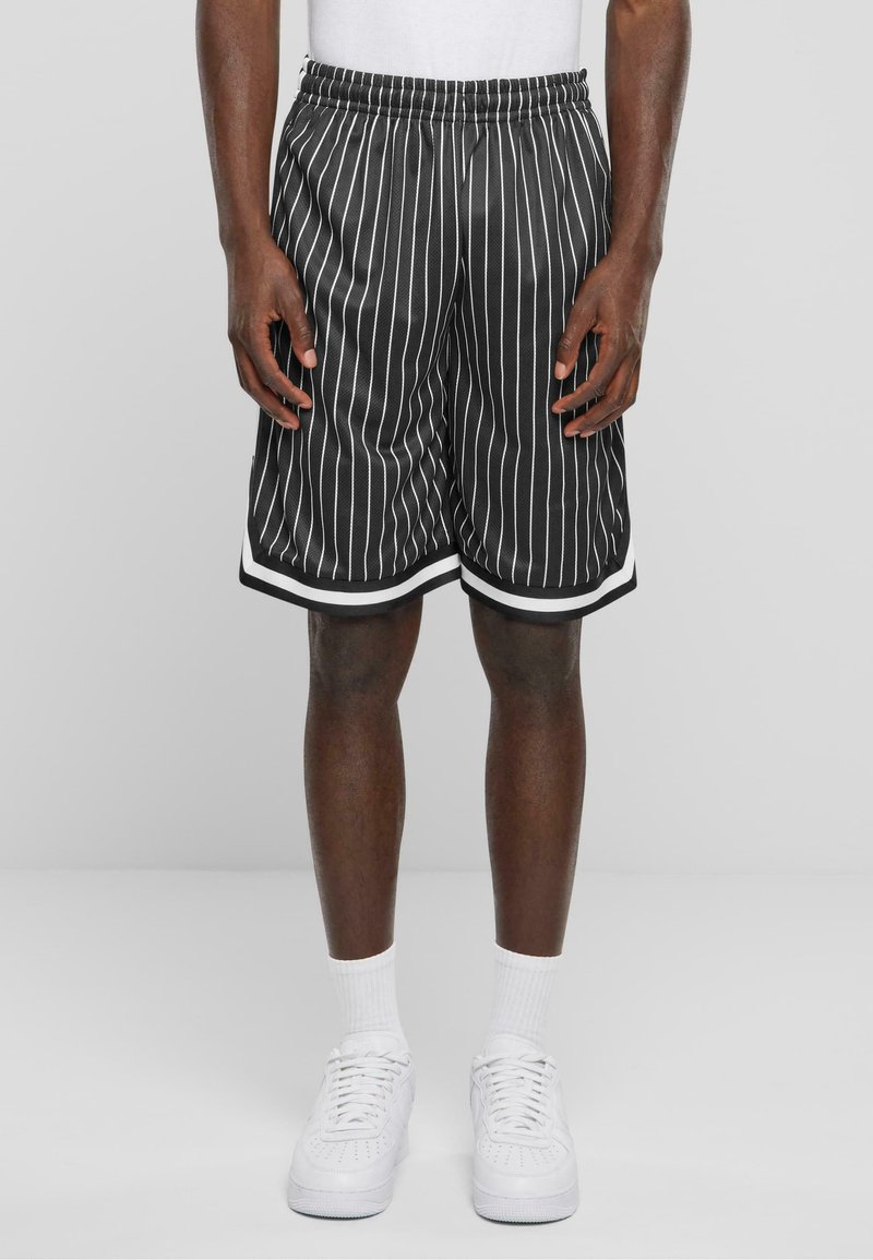 Shorts rayés noir et blanc avec une texture en maille, taille élastique et bord blanc à l'ourlet, associés à des baskets blanches et des chaussettes.