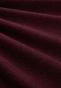 Tissu bordeaux avec une surface texturée, présentant des motifs subtils de fils entrelacés, affichant une finition douce et légèrement duveteuse.