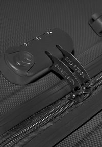 Fermeture éclair noire de valise avec deux tirettes marquées "SMARTBOX", sécurisée par une serrure à combinaison à trois chiffres sur une surface texturée.