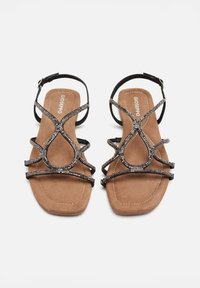 Sandalias planas negras con una plantilla texturizada marrón, que presentan tiras decorativas adornadas con pequeñas piedras de strass transparentes en un patrón.
