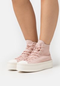 Höga sneakers i mjuk rosa mocka med vita gummikappor och kraftiga plattformssulor. Har snörning och en slät yta.
