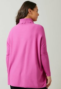 Maglione rosa con un alto colletto a costine e maniche lunghe a costine. Il tessuto è morbido e presenta una vestibilità rilassata e oversize.