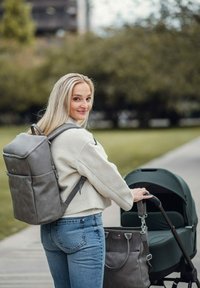 Šedý batoh z umělé kůže s nastavitelnými popruhy, vybavený horním madlem a přední kapsou, spojený s tmavě zeleným kočárkem.
