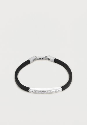 Mustast kummist käevõru, millel on väikesed kolmnurksed naastud ja hõbedane kaardus lukk.