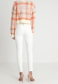 Maglione all'uncinetto con motivo a quadri rosa e beige, pantaloni bianchi a vita alta e sandali con tacco color nude. Texture morbida e design aderente.