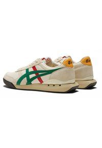 Sneaker beige con strisce verdi e rosse, superficie testurizzata, collo imbottito e suola in gomma nera; accentuazione arancione sul tallone con dettaglio del logo.
