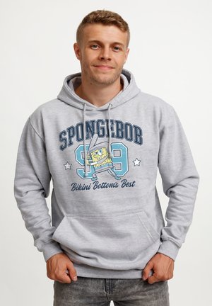 Unge mand iført en lysegrå hættetrøje med SpongeBob-figur, nummer 99 og teksten "Bikini Bottom's Best" på fronten.