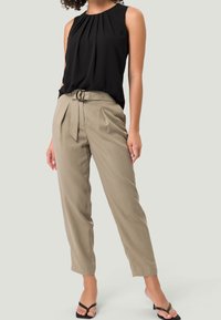 Sort ærmeløs top med plisseringer, kombineret med beige højtaljede bukser med bælte og smalle ben, suppleret med sandaler med hæl.