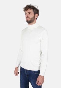 Maglione bianco a collo alto in tessuto morbido, con maniche lunghe e design aderente. Abbinato a jeans blu. Linee semplici e pulite.