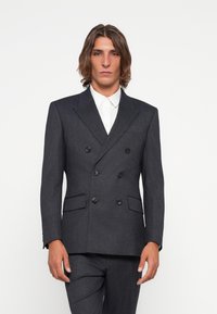 Mørk grå dobbeltrad blazer med slagkrage, to frontlommer og svarte knapper. Stylet med en hvit skjorte under.