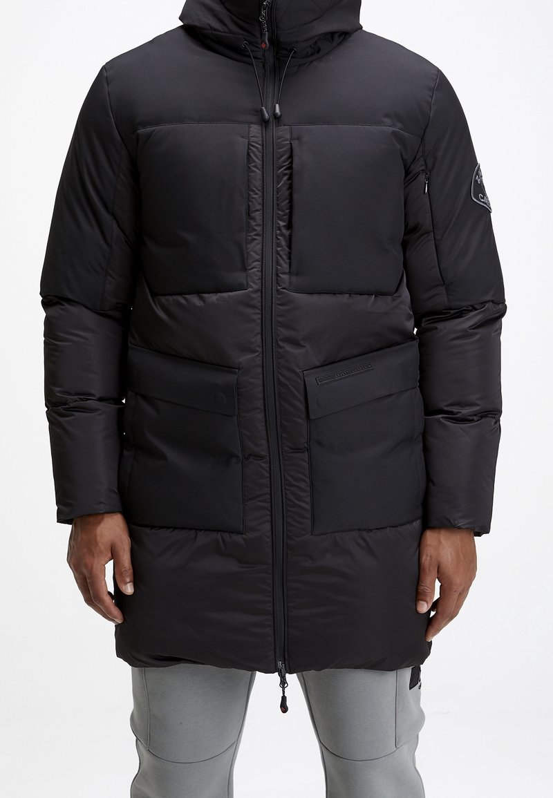 Veste matelassée noire avec capuche, fermeture zippée à l'avant et deux grandes poches. Tissu lisse et mat avec panneaux matelassés et logo embossé.