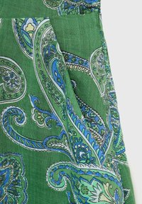 Grüner Paisley-Stoff mit komplexen blauen und weißen Mustern, einer glatten Textur und subtilen Glanz. Enthält ein Taschendetail.