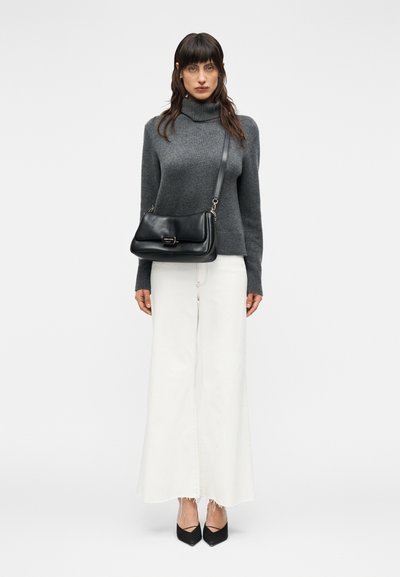 Γκρι πουλόβερ με ζιβάγκο, λευκό παντελόνι φαρδύ, μαύρη τσάντα ώμου με ασημένιο κούμπωμα και μαύρες μυτερές γόβες, σε απλό φόντο.