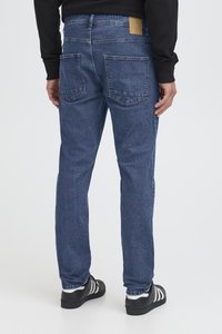 Jeans i mörkblå denim med raka ben, med två bakfickor och en brun etikett på midjebandet. Tygets textur är slät.