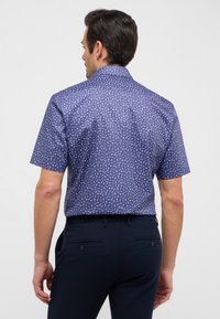 Korte mouwen shirt in donkerblauw met een klein, herhalend wit patroon. Heeft een standaard kraag en een rechte snit. Getextureerde stof.