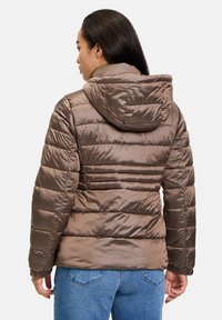 Giubbotto puffo marrone con cappuccio, caratterizzato da cuciture orizzontali e polsini elasticizzati. Indossato sopra jeans blu, che mostrano una texture liscia e lucida.