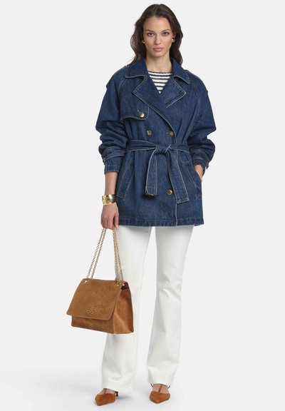 Džínový trenčkot s opaskom v páse, dvojradové zapínanie a veľkým golierom. Kombinovaný s bielymi nohavicami a hnedou semišovou kabelkou.