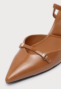 Chaussure plate marron à bout pointu avec une fine bride sur l'avant et une petite boucle à l'arrière.