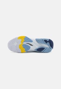 La semelle de la chaussure présente une base blanche avec des accents jaunes, bleus et navy. Des grips texturés améliorent l'adhérence. Le caoutchouc texturé assure la durabilité.